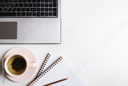 Laptop computer, green tea in a pink cup, notebooks with clean pages and metal pen on white table. Office desk flat lay