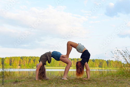 two girls do gymnastic exercises outdoor in a picturesque place by the river and having fun