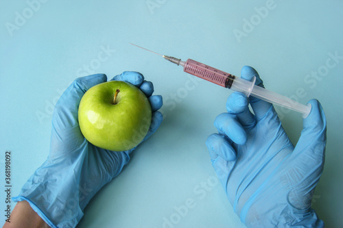Green apple and syringe with GMO in hands on a blue background.