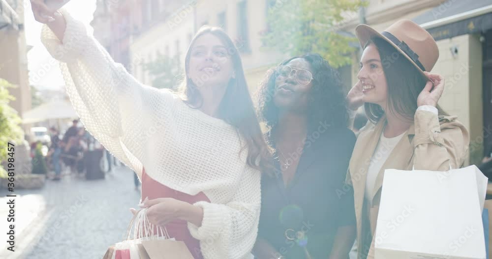 Portrait of multi-ethnic women posing outdoors. Pretty Caucasian girl making selfie photos on smartphone while standing in city with friends. Happy African American woman smiling to phone camera Portrait of multi-ethnic women posing outdoors. Pretty Caucasian girl making selfie photos on smartphone while standing in city with friends. Happy African American woman smiling to phone camera