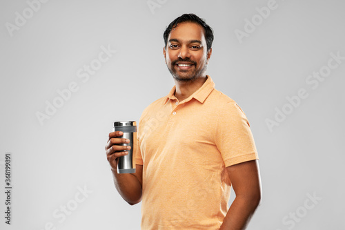 eco living and sustainability concept - happy smiling young indian man in polo t-shirt with thermo cup or tumbler for hot drinks over grey background