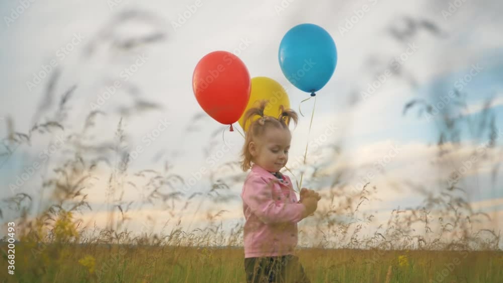 A little lovely girl, a happy child running on the green grass with colorful balloons in her hands. The concept of freedom, a child's dream, a happy family. A little lovely girl, a happy child running on the green grass with colorful balloons in her hands. The concept of freedom, a child's dream, a happy family.
