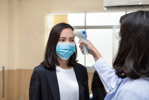Doctor check Asian woman body temperature using infrared forehead thermometer for virus symptom at hospital. Corona virus, Covid-19, quarantine or virus outbreak concept