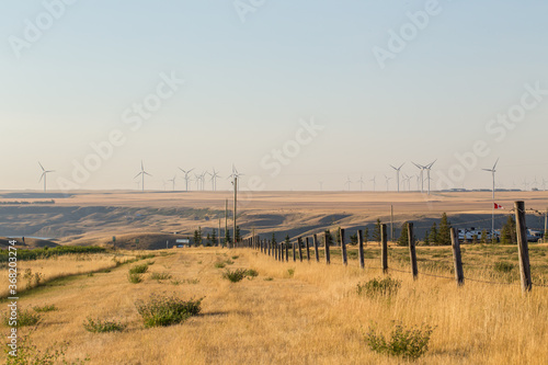 Windmill in the distance in Alberta Prairies. Wind farm power as an alternative energy source with fence in foreground. Energy development and power generation. Wind Turbines and power generation.