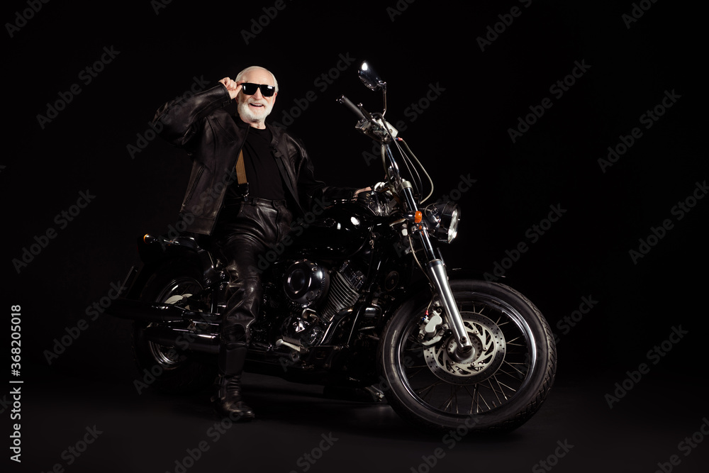Portrait of his he nice attractive content cheerful grey-haired guy dude hipster traveler sitting on chopper spending weekend holiday tour trip touching specs isolated black color background