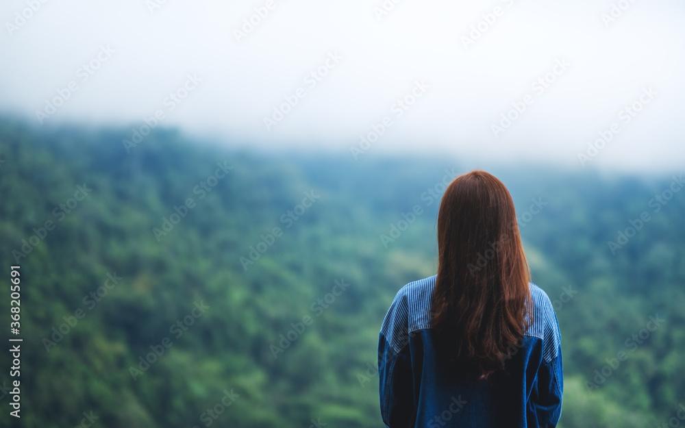 Rear view image of a female traveler looking at a beautiful green mountain on foggy day