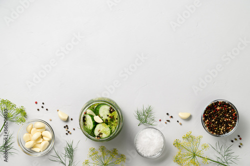 Healthy probiotic vegan food. Homemade fermented cucumbers with garlic, dill and pepper in a glass jar. Light gray concrete background. Top view, copy space.