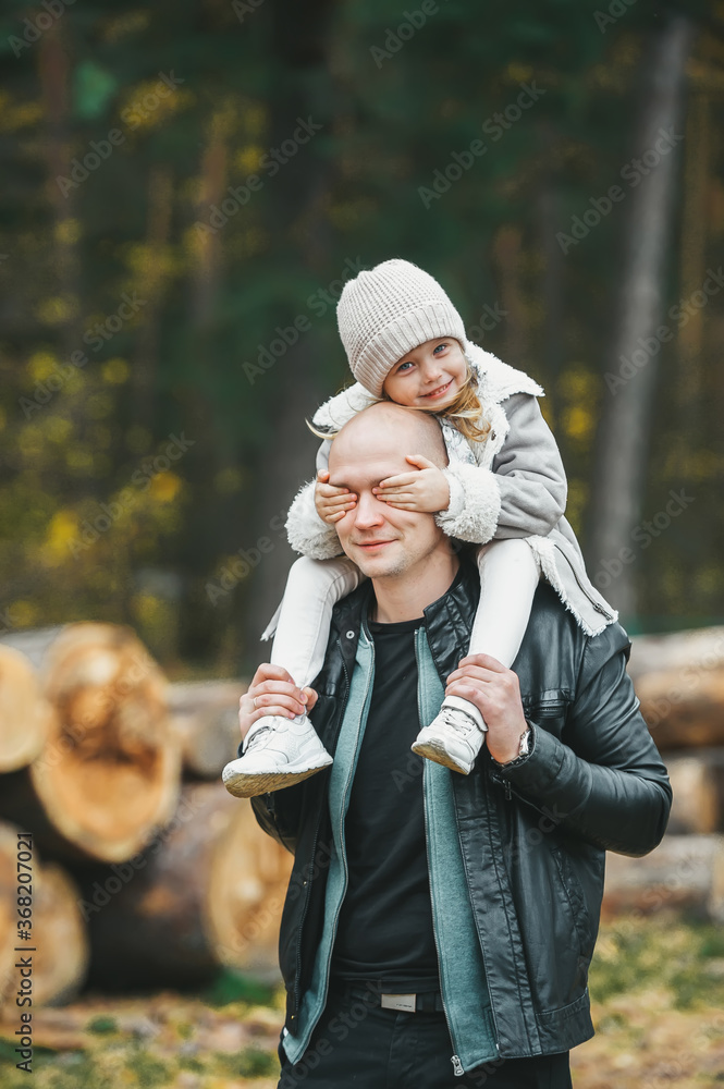 Happy cheerful little daughter playing covering daddy eyes with hands in autumn forest.