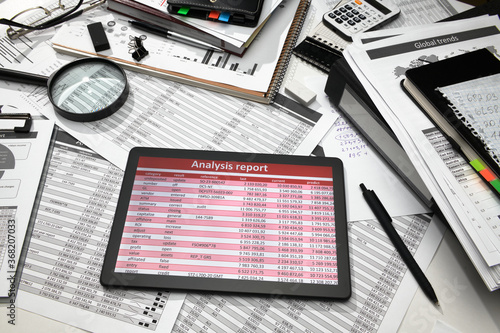 business office desk closeup - tablet computer with tables and graphs on the screen, financial reports, analysis and accounting, set of documents for bookkeeping