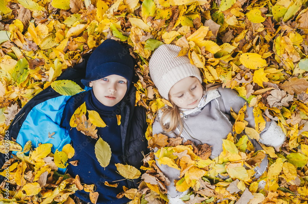 Little brother and sister lie on their backs in yellow leaves. Happy children in autumn park lying on leaves. Little brother and sister lie on their backs in yellow leaves. Happy children in autumn park lying on leaves.