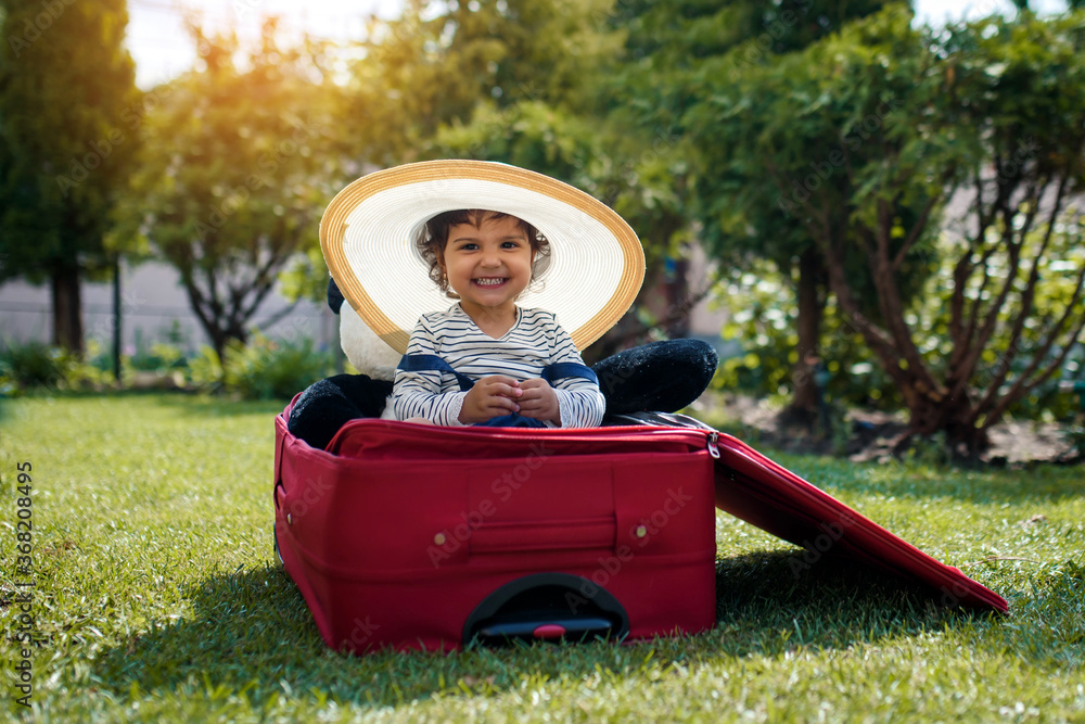 A happy little girl is sitting in the suitcase on the gras and shaking hands. A happy little girl is sitting in the suitcase on the gras and shaking hands.