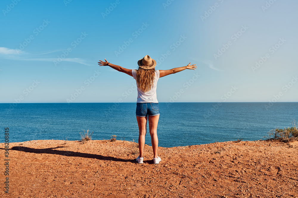 Young woman with open arms and hat in front of the sea in summer Concept of travel, holidays and adventure.