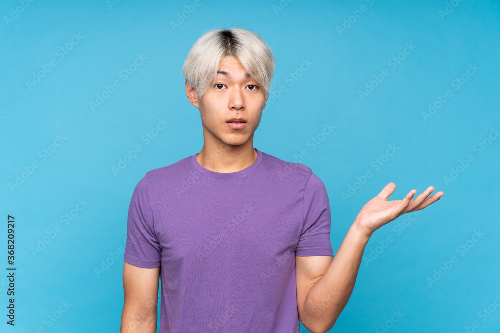 Fototapeta premium Young asian man over isolated blue background making doubts gesture