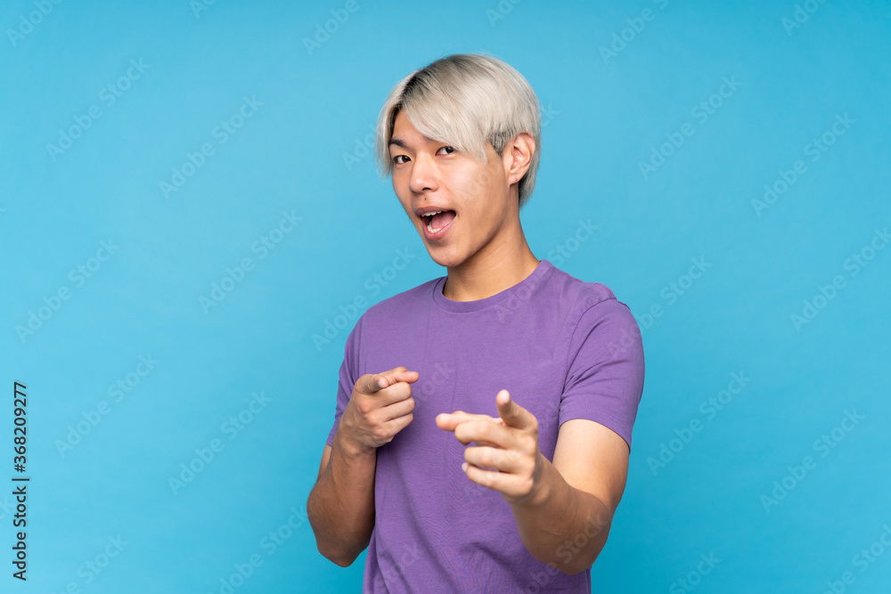 Young asian man over isolated blue background pointing to the front and smiling Young asian man over isolated blue background pointing to the front and smiling