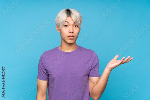 Young asian man over isolated blue background making doubts gesture
