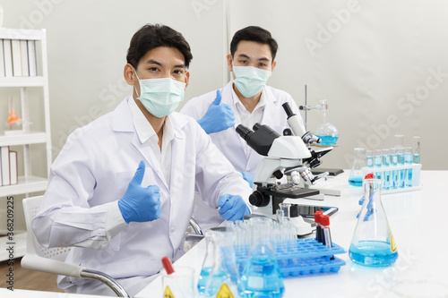 Two Male Scientists wear Face Mask working in Lab while show thumb Up and Ready to Work and Presentation.  Blue Tone. SARS-CoV-2 , Covid-19 THEME.