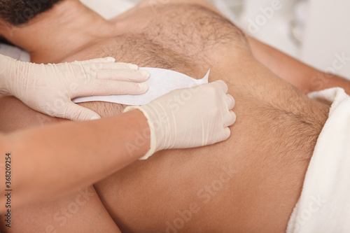 Cosmetologist doing waxing on torso of unrecognizable male client photo