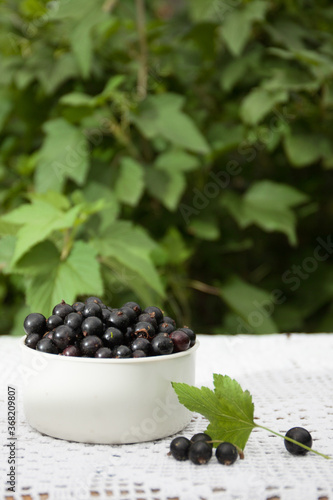 shiny, delicious and fresh black currant in a white Cup on a Lacy rustic tablecloth on a wooden background