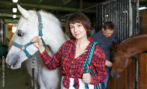 Portrait of cheerful woman horse farm worker standing at stable