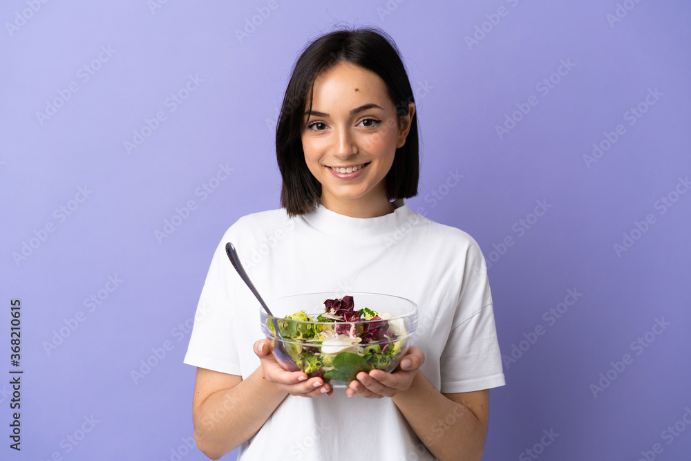 Young caucasian woman isolated on purple background holding a bowl of salad with happy expression