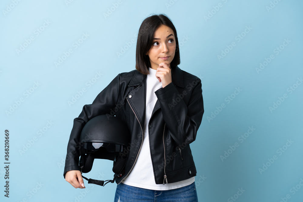 Woman holding a motorcycle helmet isolated on blue background and looking up Woman holding a motorcycle helmet isolated on blue background and looking up
