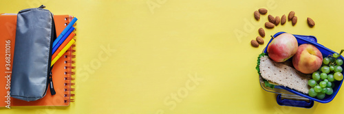 Large yellow background with school lunch with crispbreads with lettuce and cheese, apple, peach, grapes and almonds. Healthy school lunch. A healthy lunch box on a yellow background with free space.