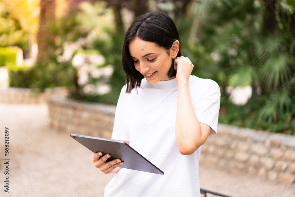 Fototapeta premium Young caucasian woman holding a tablet at outdoors