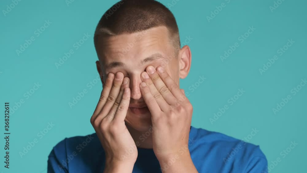 Portrait of young man tiredly rubbing eyes on camera over colorful background Portrait of young man tiredly rubbing eyes on camera over colorful background
