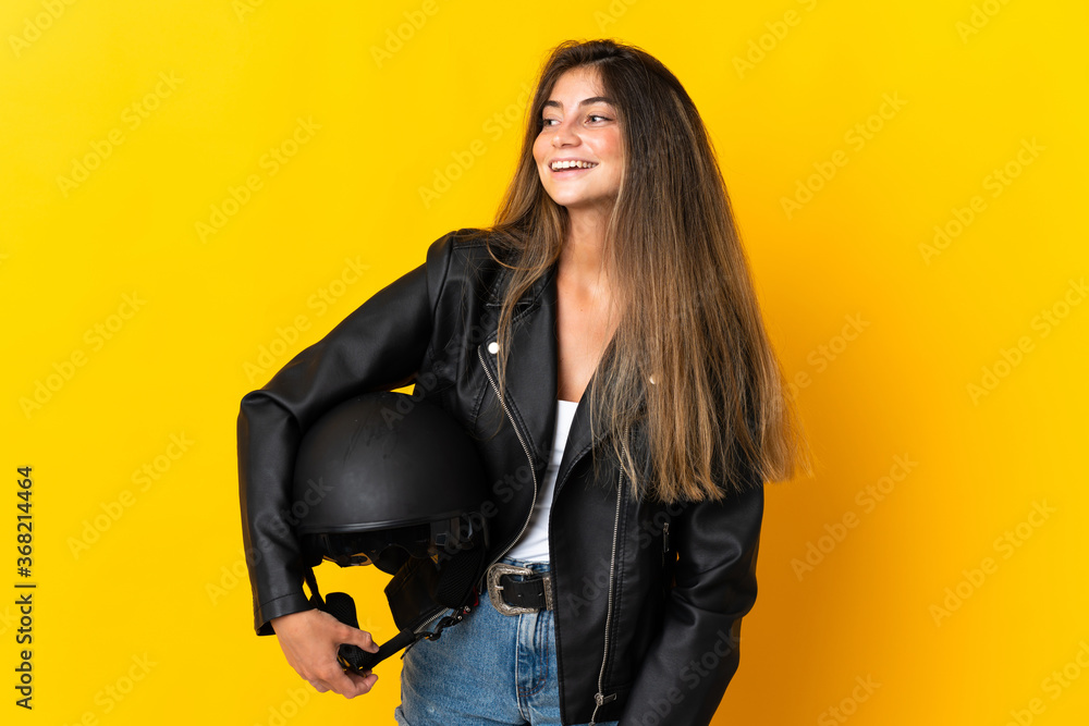 Woman holding a motorcycle helmet isolated on yellow background looking to the side and smiling Woman holding a motorcycle helmet isolated on yellow background looking to the side and smiling