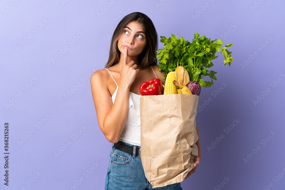 Young woman holding a grocery shopping bag having doubts while looking up Young woman holding a grocery shopping bag having doubts while looking up