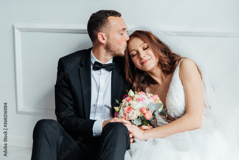 The first meeting of the groom in a black suit and the bride in a white wedding dress with a bouquet in the interior of a photo studio on a white and black background The first meeting of the groom in a black suit and the bride in a white wedding dress with a bouquet in the interior of a photo studio on a white and black background