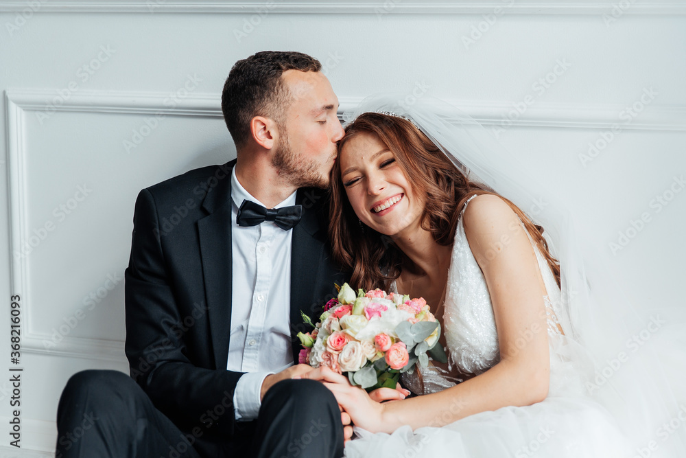 The first meeting of the groom in a black suit and the bride in a white wedding dress with a bouquet in the interior of a photo studio on a white and black background The first meeting of the groom in a black suit and the bride in a white wedding dress with a bouquet in the interior of a photo studio on a white and black background