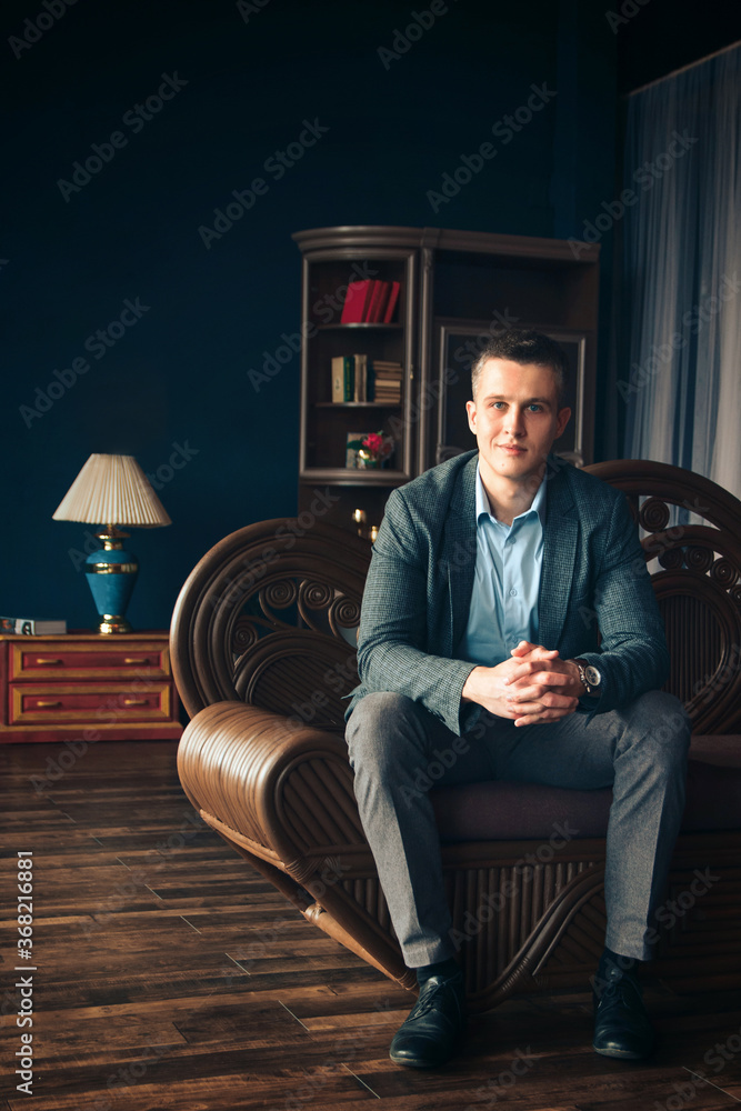 man in a blue shirt smiles while sitting on a couch, hands resting on his knees and hands clasped in a castle man in a blue shirt smiles while sitting on a couch, hands resting on his knees and hands clasped in a castle