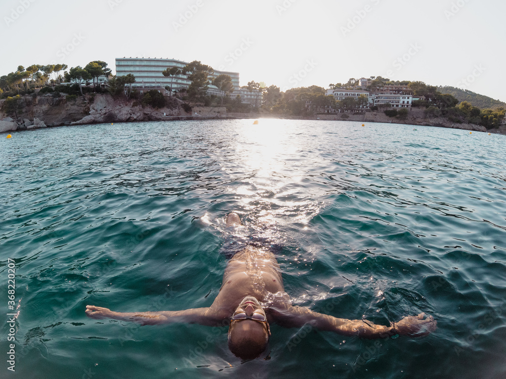 Relaxed man lying floating in the water at sunset in Majorca. Holidays, summer, vacation concept
