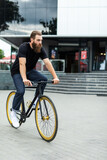 Confident young bearded man looking forward while riding on his bicycle along the street