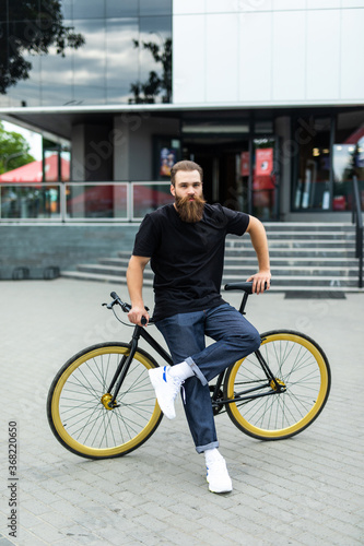Fototapeta Naklejka Na Ścianę i Meble -  Enjoying his ride. Confident young bearded man looking forward while riding on his bicycle along the street