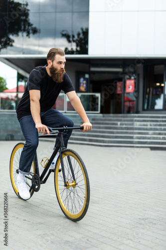 Confident young bearded man looking forward while riding on his bicycle along the street