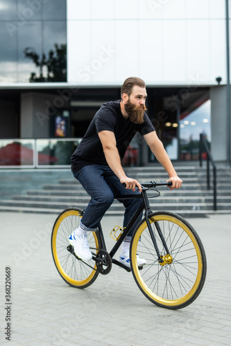 Enjoying his ride. Confident young bearded man looking forward while riding on his bicycle along the street