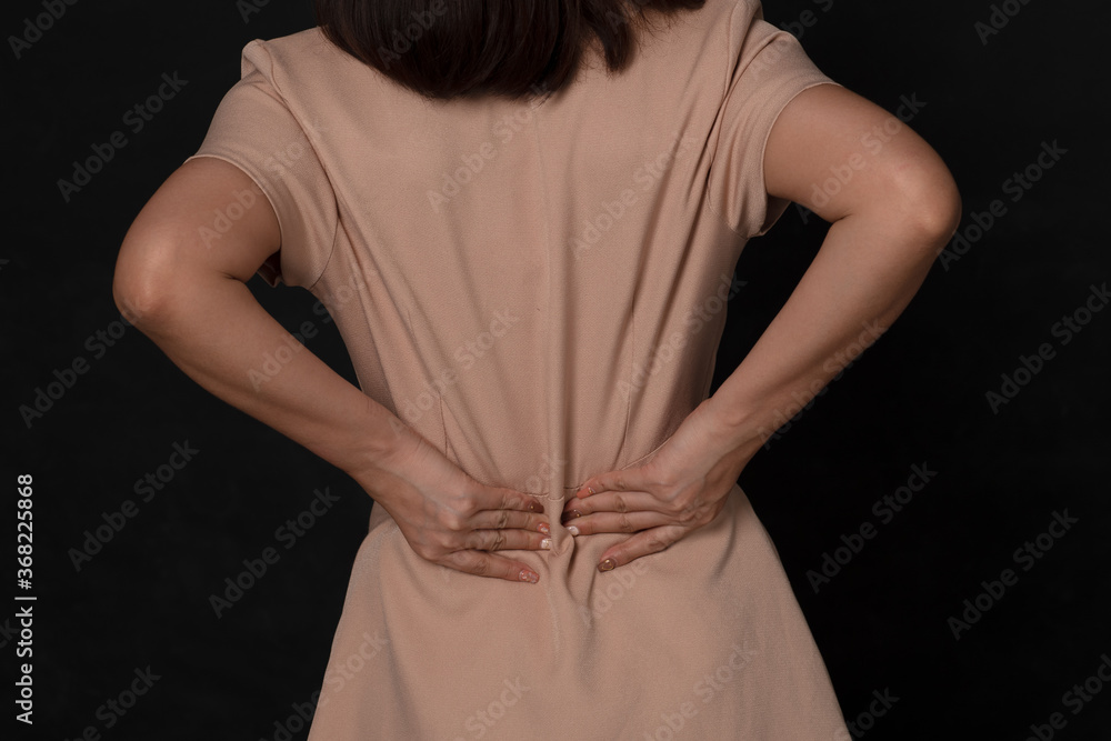 Backache concept bending over in pain with hands holding lower back on black background; Injured business woman with lower back spinal pain. Free from copy space. Backache concept bending over in pain with hands holding lower back on black background; Injured business woman with lower back spinal pain. Free from copy space.