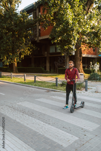 Full length of handsome young bearded caucasian man on e scooter crosses a pedestrian in the city