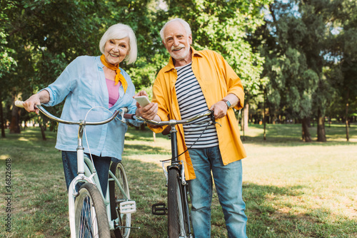 Selective focus of senior couple with smartphone smiling at camera near bikes in park © LIGHTFIELD STUDIOS