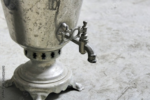One old worn steel samovar on a gray concrete floor.