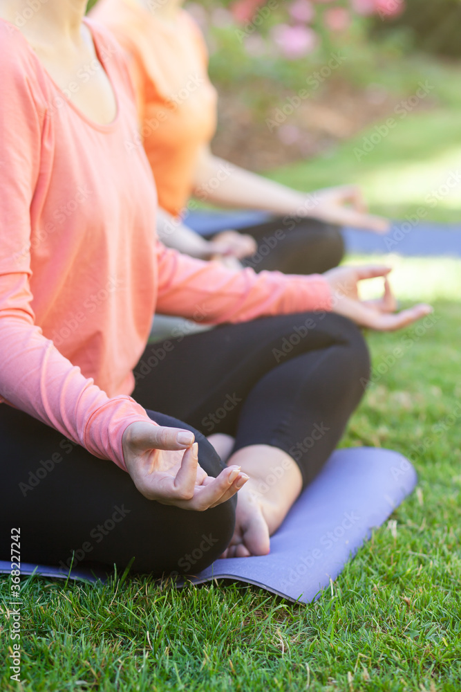 Yoga practice ourside in the park on a sunny summer morning. Two young girls sitting in lotus pose doing after workout meditation. Healthy lifestyle. Green grass on background, soft morning light Yoga practice ourside in the park on a sunny summer morning. Two young girls sitting in lotus pose doing after workout meditation. Healthy lifestyle. Green grass on background, soft morning light