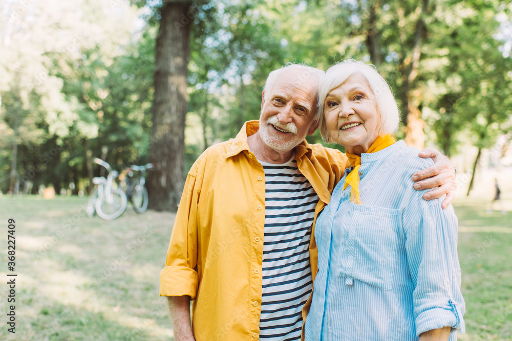 Positive senior man hugging smiling wife in summer park