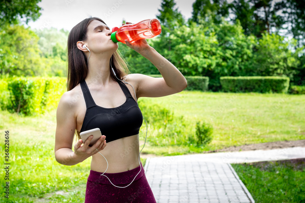 Fitness young woman in sportwear drinks water in park after training Fitness young woman in sportwear drinks water in park after training