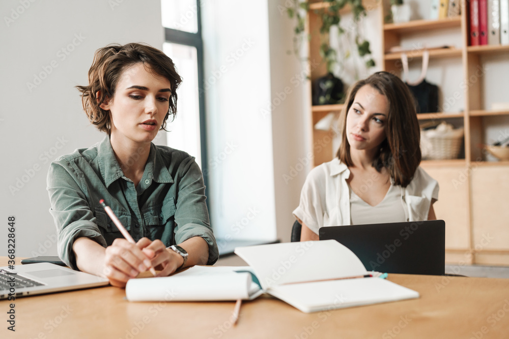 Image of young focused colleagues discussing project while working Image of young focused colleagues discussing project while working