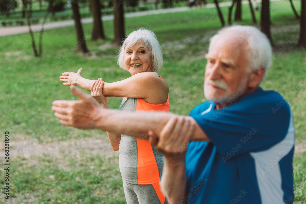 Fototapeta premium Selective focus of smiling senior woman exercising with husband in park