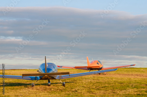 Two Light small plane on the grass on a background of blue clouds. Blur.