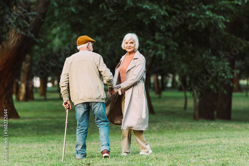 Senior woman looking at camera while walking with husband in park