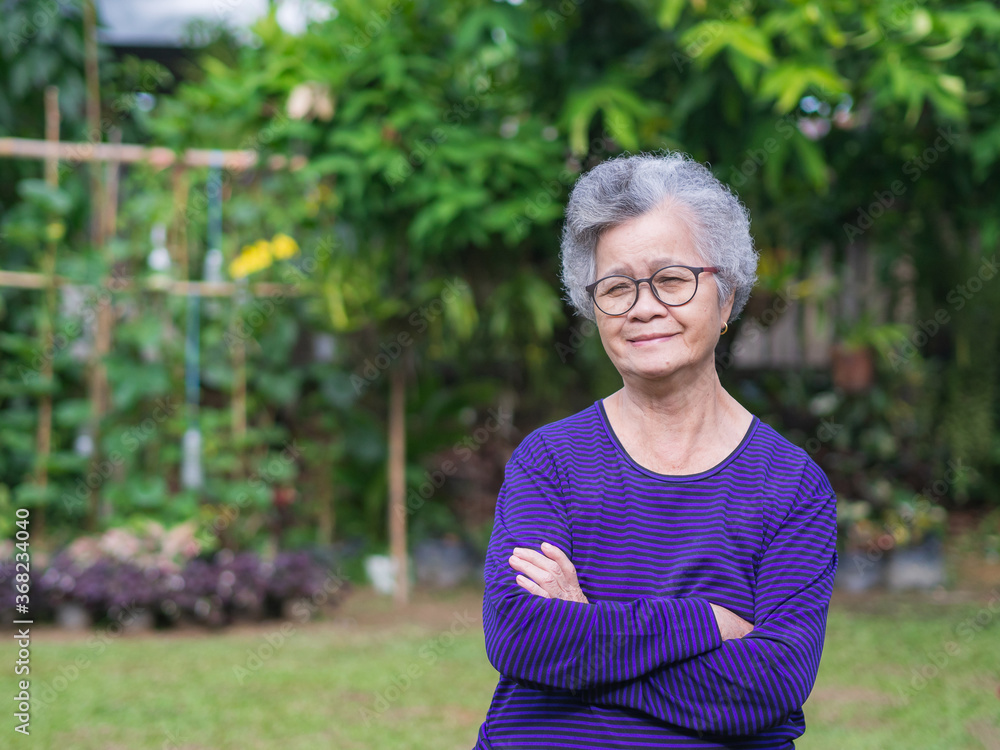 A portrait of an senior woman arms crossed while standing in a garden A portrait of an senior woman arms crossed while standing in a garden